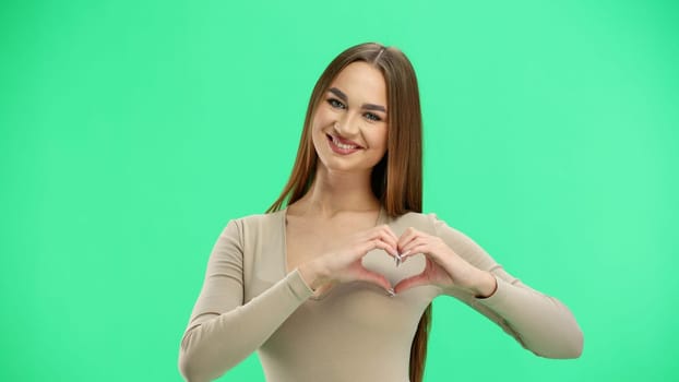 A woman, close-up, on a green background, shows a heart.