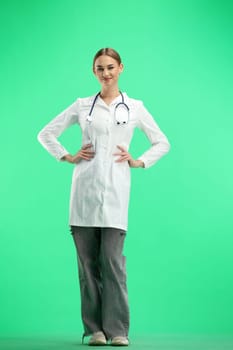 Female doctor, full-length, on a green background, hands on hips.
