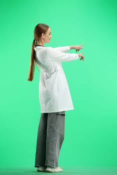 A full-length female doctor, on a green background, points forward.