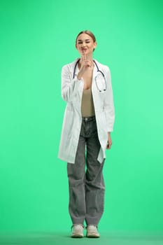 A full-length female doctor, on a green background, shows a sign of silence.