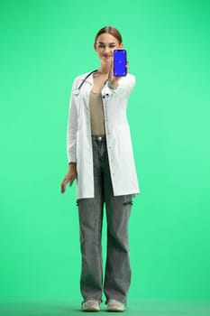 A woman doctor, full-length, on a green background, with a phone.
