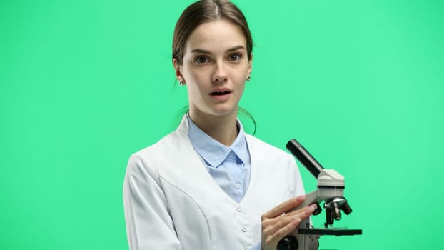 Female doctor, close-up, on a green background, with a microscope.