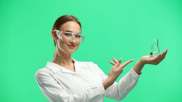 Female doctor, close-up, on a green background, holding a bottle.