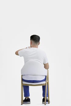 A man, full-length, on a white background, sitting on a chair.