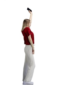 A woman, full-length, on a white background, waving her phone.