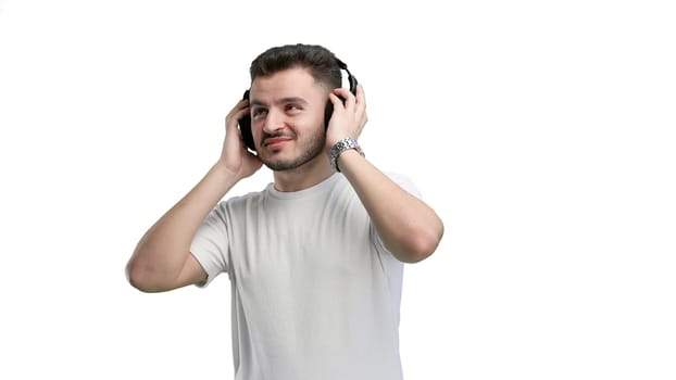 A man, close-up, on a white background, listening to music with headphones.
