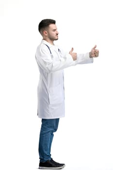 The doctor, in full height, on a white background, shows a thumbs up.