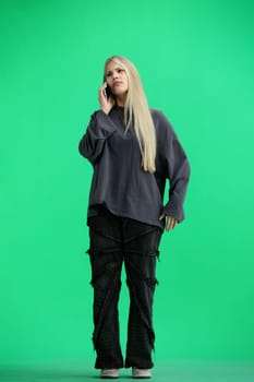 A woman, full-length, on a green background, talking on the phone.