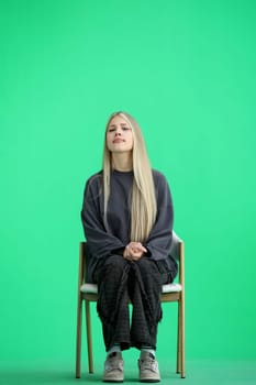 A woman, full-length, on a green background, sitting on a chair.