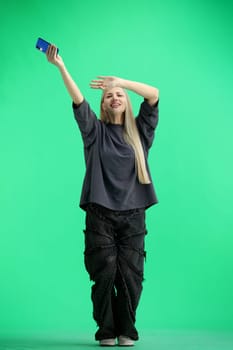 A woman, full-length, on a green background, waving her phone.