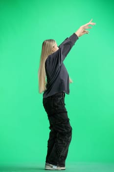 A woman, full-length, on a green background, waving her hand.