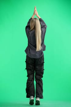 A woman, full-length, on a green background, raised her hands up.