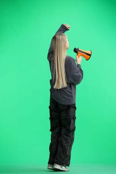 A woman, full-length, on a green background, with a megaphone.