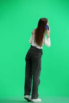 A woman, full-length, on a green background, talking on the phone.