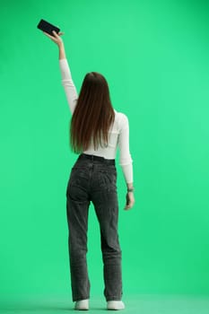 A woman, full-length, on a green background, waving her phone.