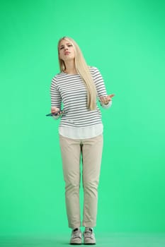 A woman, full-length, on a green background, uses a phone.
