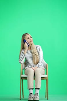 A woman, full-length, on a green background, sitting on a chair.