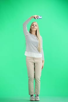 A woman, full-length, on a green background, waving her phone.