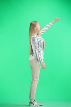 A woman, full-length, on a green background, raised her hand up.