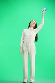 A woman, full-length, on a green background, waving her phone.