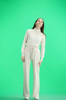 A woman, full-length, on a green background, looks into the distance.