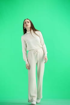 A woman, full-length, on a green background, looks into the distance.