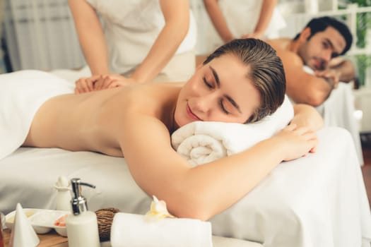 Caucasian couple customer enjoying relaxing anti-stress spa massage and pampering with beauty skin recreation leisure in day light ambient salon spa at luxury resort or hotel. Quiescent