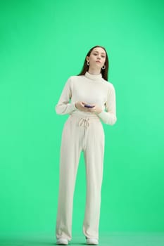 A woman, full-length, on a green background, uses a phone.