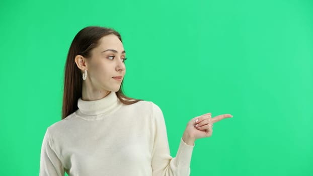 A woman, close-up, on a green background, points to the side.
