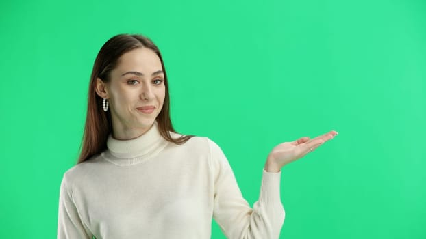 A woman, close-up, on a green background, points to the side.