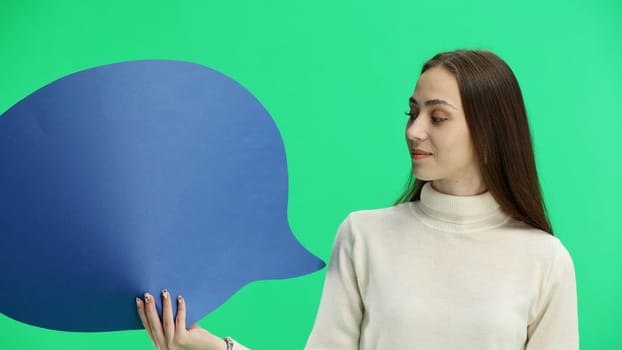 A woman, close-up, on a green background, shows a blue comment sign.