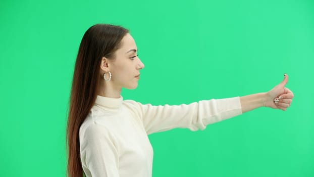 A woman, close-up, on a green background, shows her thumbs up.