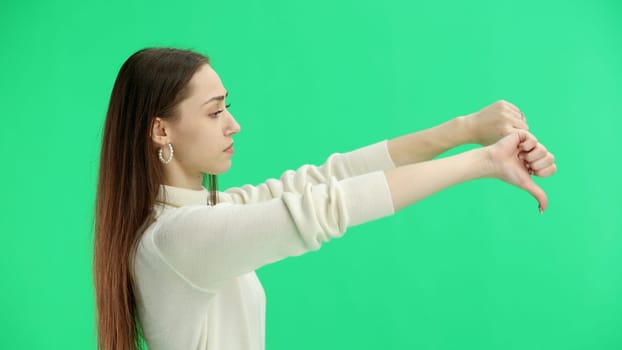 A woman, close-up, on a green background, shows her thumbs down.