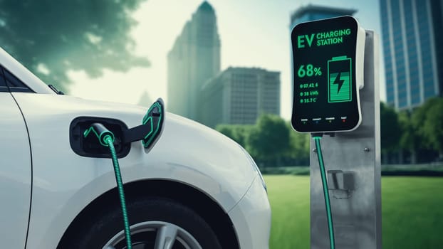 Electric car plug in with charging station to recharge battery with electricity by EV charger cable in eco green city park. Future innovative EV car using alternative clean energy reducing CO2. Peruse