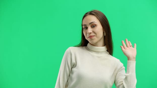 A woman, close-up, on a green background, waving her hand.