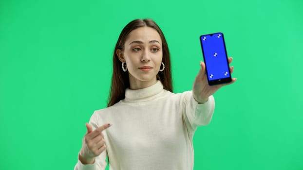 A woman, close-up, on a green background, shows a phone.