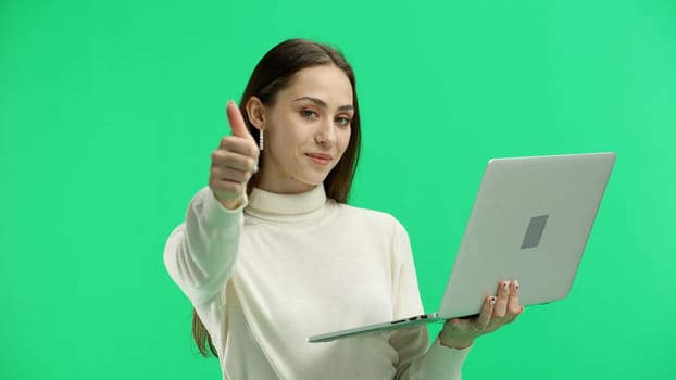 A woman, close-up, on a green background, uses a laptop.