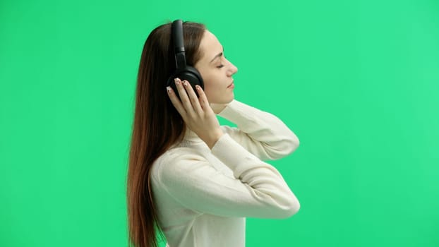 A woman, close-up, on a green background, listening to music with headphones.