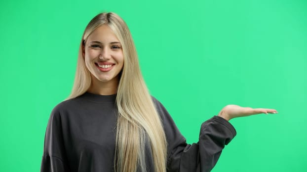 A woman, close-up, on a green background, points to the side.