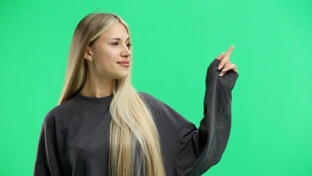 A woman, close-up, on a green background, points to the side.