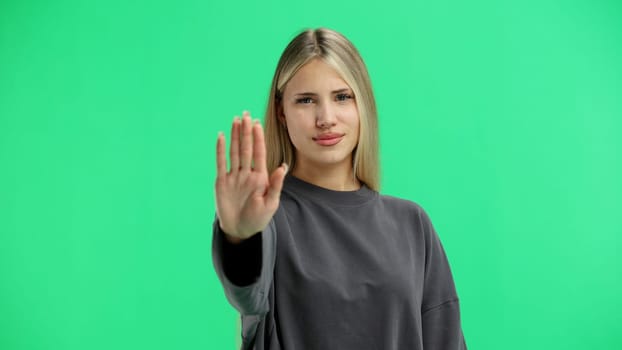 A woman, close-up, on a green background, shows a stop sign.