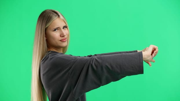 A woman, close-up, on a green background, shows her thumbs down.