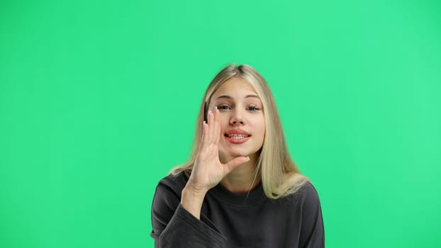 A woman, close-up, on a green background, tells a secret.