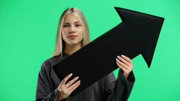 A woman, in close-up, on a green background, points an arrow to the side.