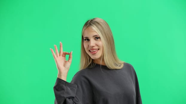 A woman, close-up, on a green background, shows an ok sign.
