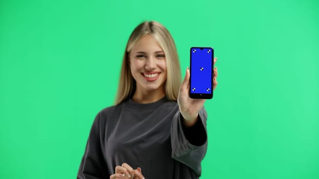 A woman, close-up, on a green background, shows a phone.