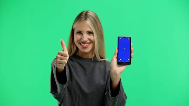 A woman, close-up, on a green background, shows a phone.