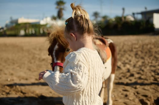 Rear view of a Caucasian little child girl with a pony on the sandy beach