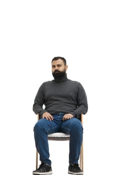A man, full-length, on a white background, sitting on a chair.