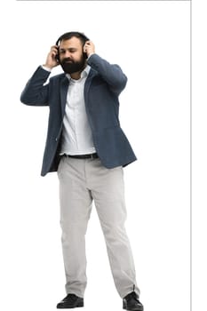 A man, full-length, on a white background, listening to music with headphones.